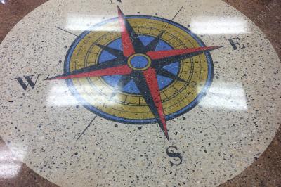Blue, red, and gold colored compass rose surrounded by a circle of natural concrete with a brown field on a polished concrete floor using 3.4 mil vinyl stencil and Ameripolish dye.
