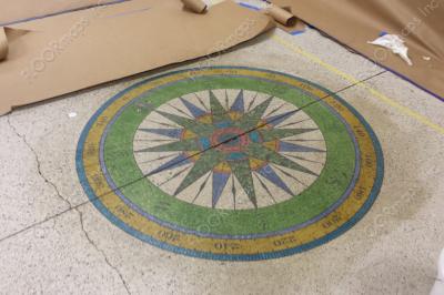 Green, gold, and blue compass rose installed on a polished concrete floor using 3.4 mil vinyl stencil and Ameripolish dye.