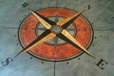 Orange, black, and gold colored compass rose surrounded by a blue field on a concrete overlay using 3.4 mil vinyl stencil and skimstone stain.